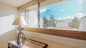 Ein Zimmer mit großem Fenster, einem Tisch mit Lampe und Blick auf eine verschneite Landschaft.