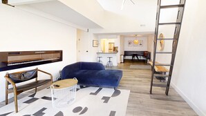 A modern living room with a blue sofa, a wooden coffee table, a black leather bench, a white wire basket, and a large rug with abstract patterns. - Modern & chic year-round getaway with mountain views & fireplace- near shopping (Park City)
