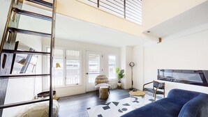 A spacious living area with a blue sofa, a white armchair, a wooden ladder, and a large window. - Modern & chic year-round getaway with mountain views & fireplace- near shopping (Park City)