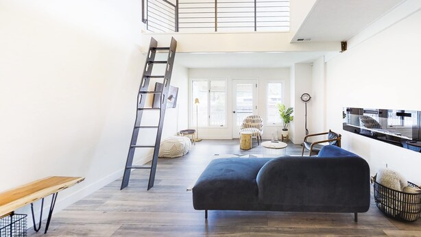 A spacious living area with a dark-colored sofa, a wooden bench, a ladder, and a staircase leading to an upper level. - Modern & chic year-round getaway with mountain views & fireplace- near shopping (Park City)