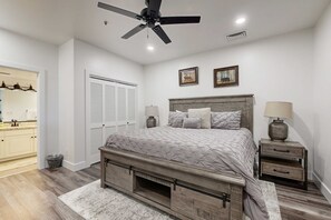 Ein Schlafzimmer mit Bett, Nachttischen, Deckenventilator, einer Tür und einem an der Wand hängenden Bild.