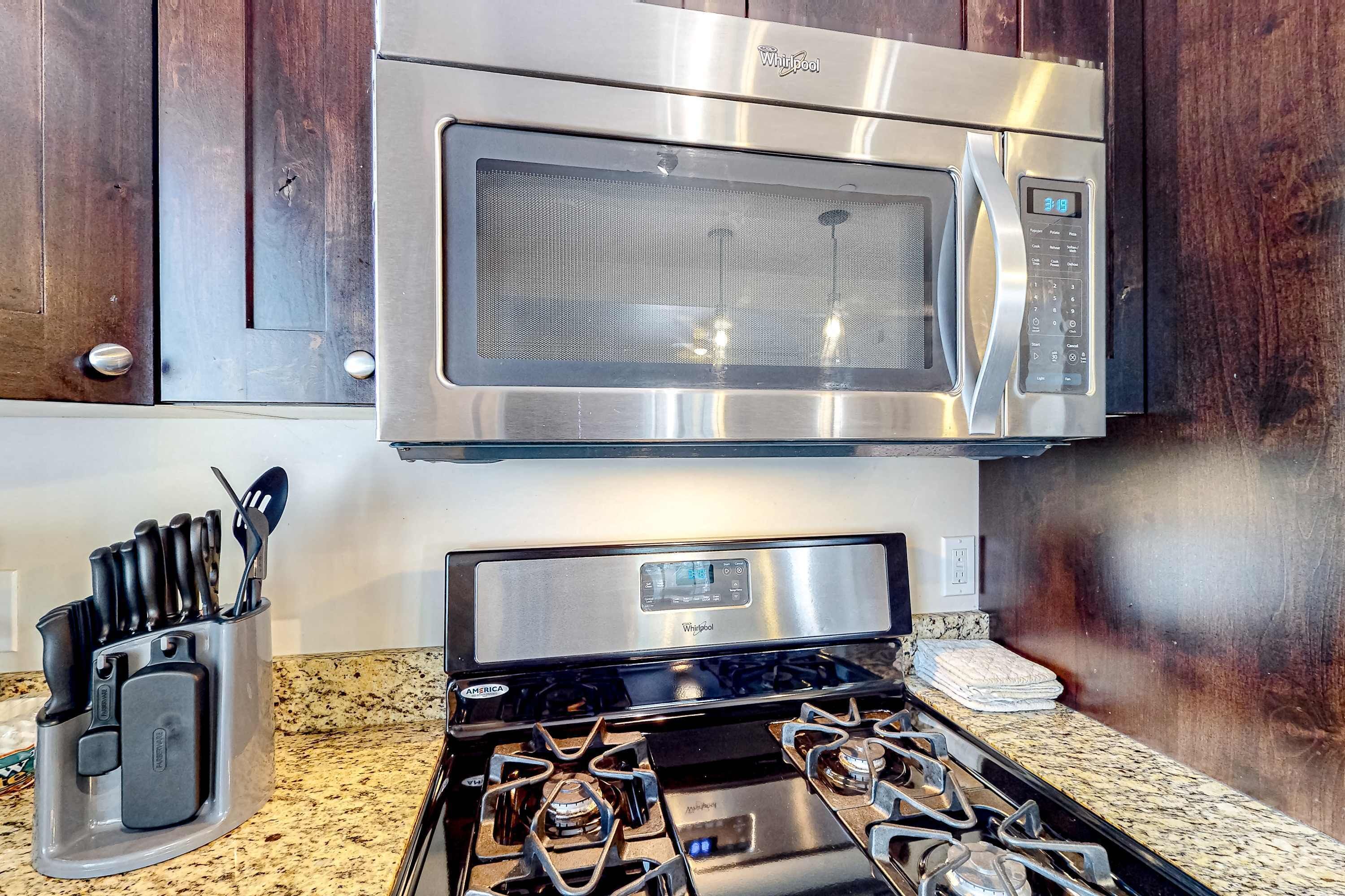 A kitchen with a stainless steel microwave, a stove with four burners, and a knife block.