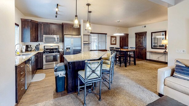 A modern kitchen with stainless steel appliances, a central island, and pendant lighting. - Light-filled condo near Canyons Village with mountain view, pool & hot tubs (Park City)