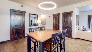 A dining area with a wooden table and chairs, a modern pendant light, and a sofa in the adjacent living room. - Light-filled condo near Canyons Village with mountain view, pool & hot tubs (Park City)