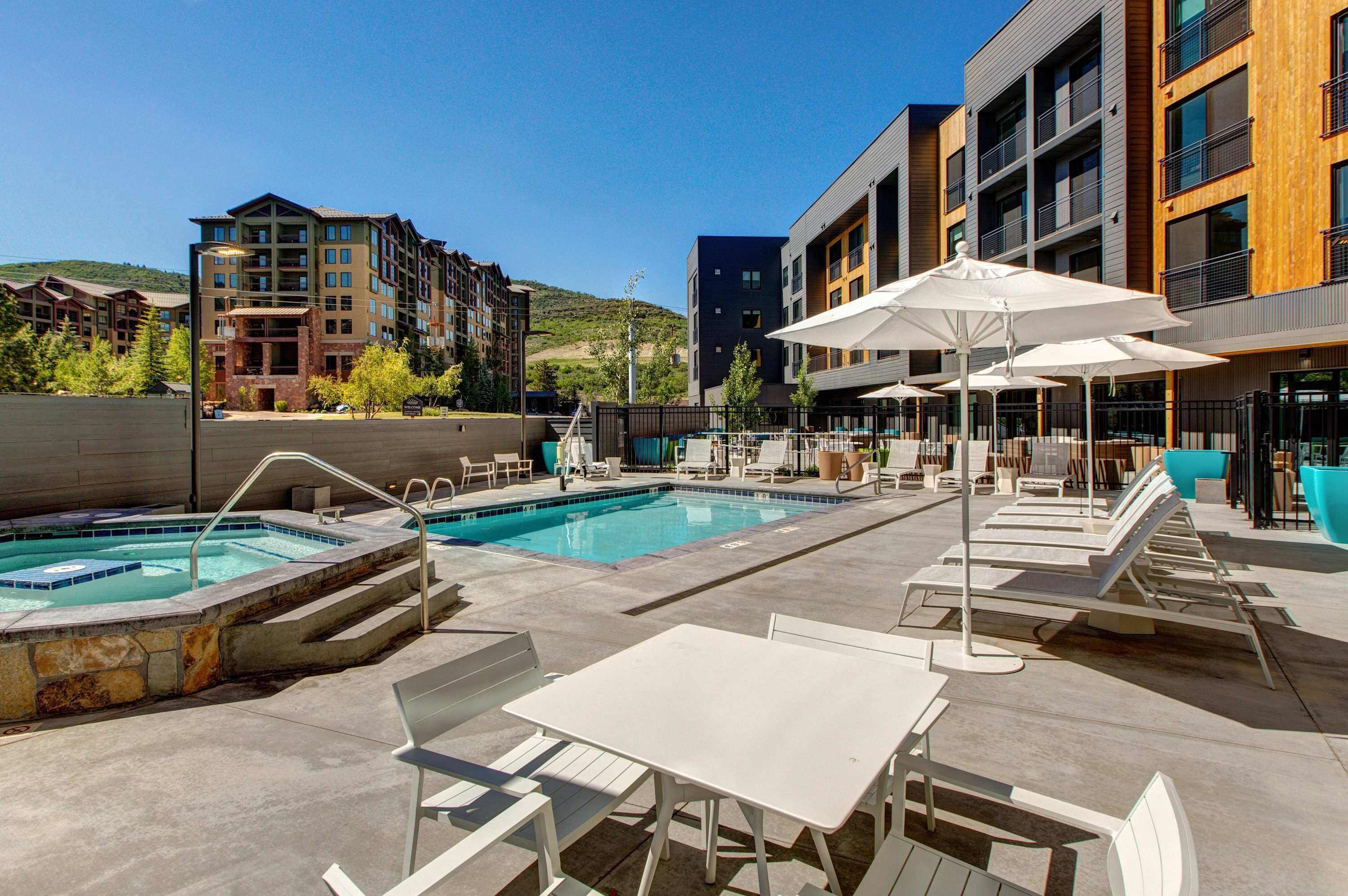 A rooftop pool area with lounge chairs, tables, and umbrellas.