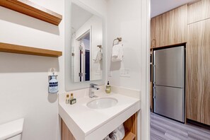 Un baño moderno con un lavamanos blanco, espejo y estantes de madera.
