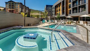 Piscina com área para banhos de sol, espreguiçadeiras e vista para edifícios próximos.