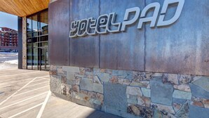 Entrada de hotel com fachada de pedra, uma placa moderna e visão clara do estacionamento.
