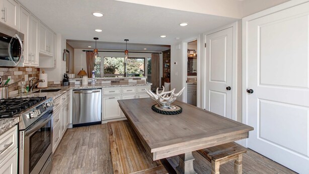 A modern kitchen with white cabinetry, stainless steel appliances, and a wooden dining table. - Three-story townhome with private hot tub, gas fireplace, decks (Park City)