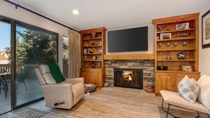 A living room with a fireplace, a television mounted above it, and a bookshelf filled with various items. - Three-story townhome with private hot tub, gas fireplace, decks (Park City)