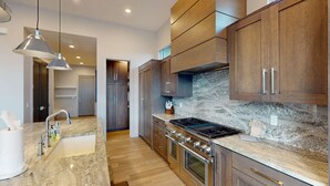 Eine moderne Küche mit Marmorarbeitsplatte, Edelstahlgeräten, Holzausbau und Pendelleuchten.