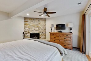 Ein Schlafzimmer mit Bett, Steinwand, Kamin, Holzkommode, Fernseher und Deckenventilator.