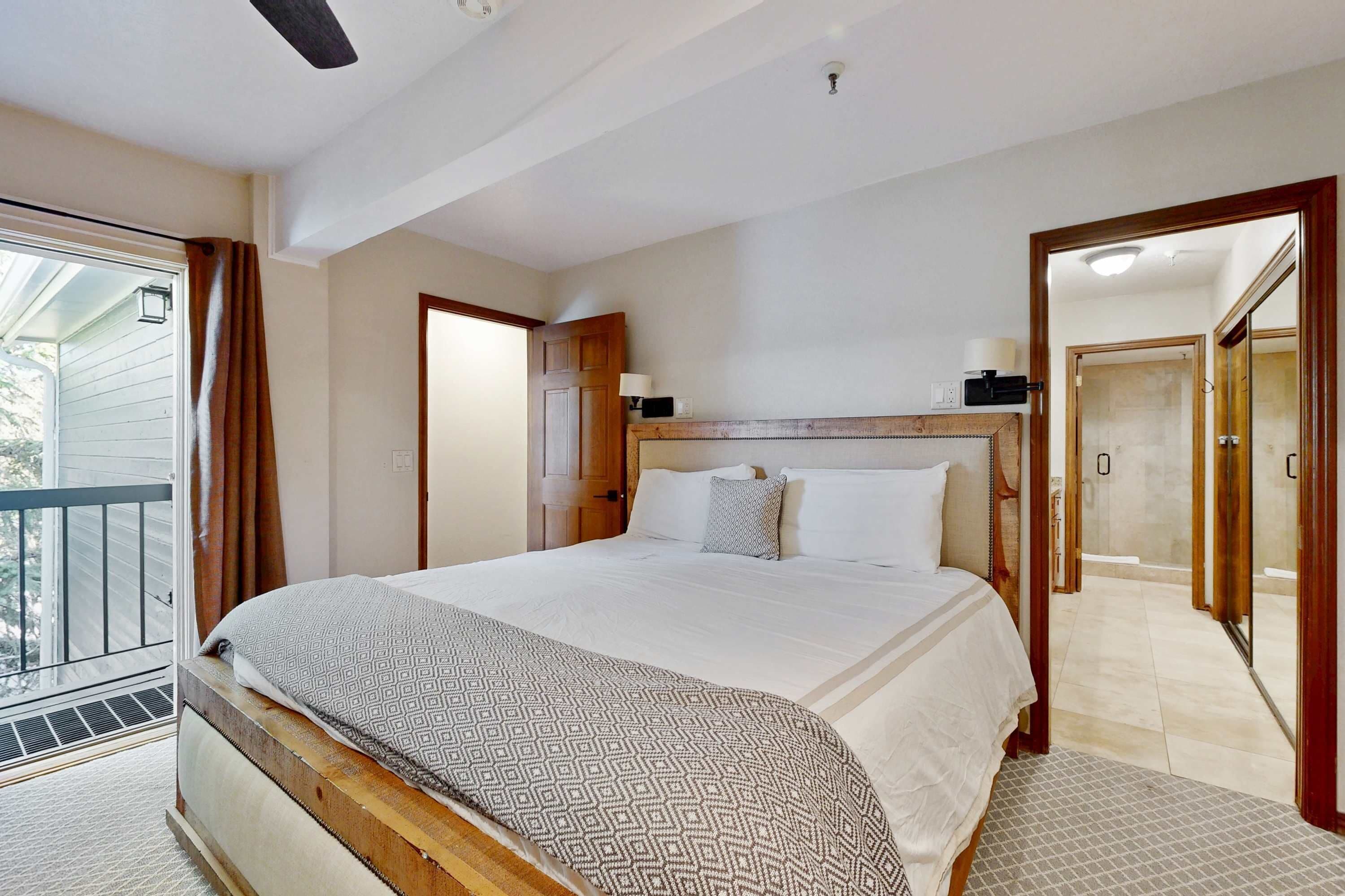 Een slaapkamer met een groot bed, een houten hoofdbord, een balkon en een badkamer met douche en toilet.