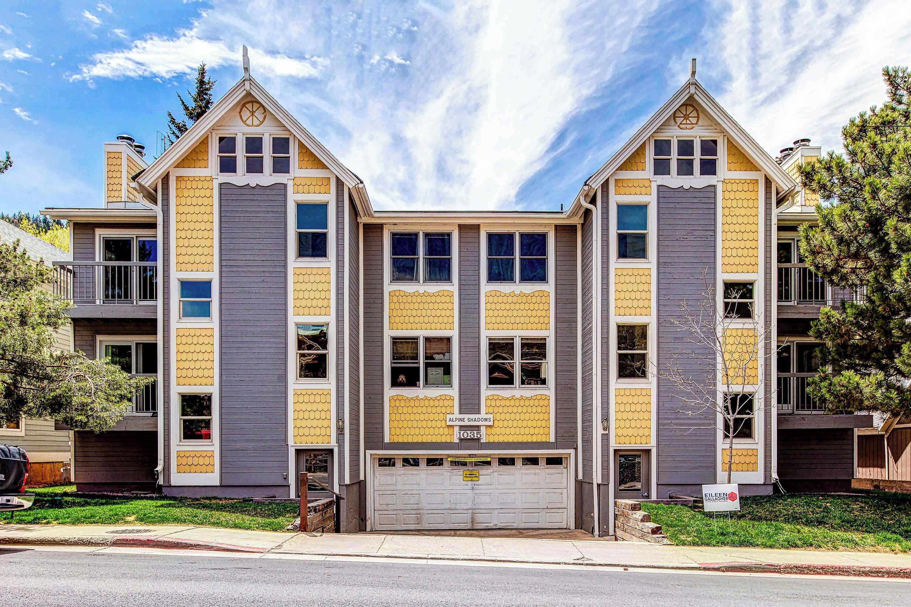 Un bâtiment à deux étages avec un garage, une enseigne indiquant « Alpine Shadows » et une pancarte « À vendre ».