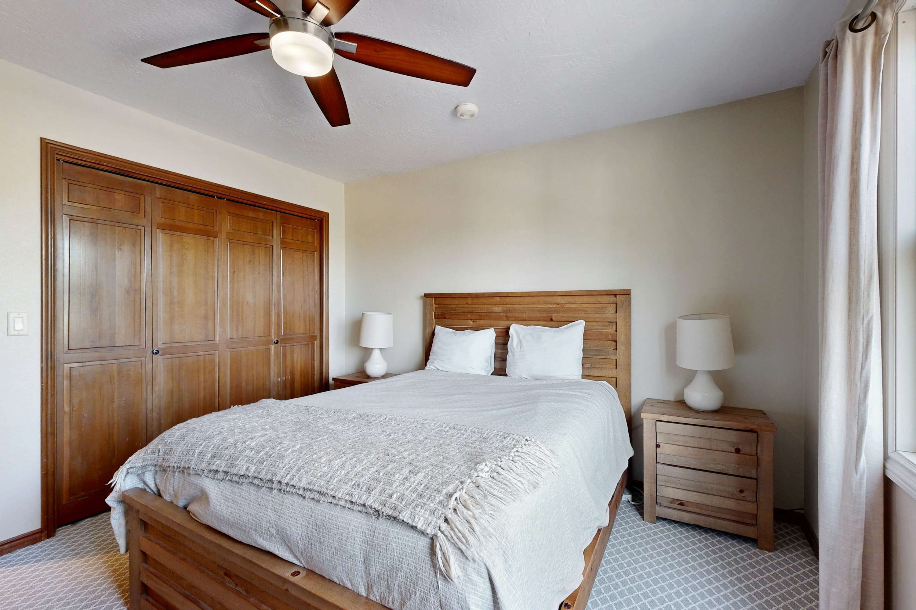Une chambre à coucher avec un lit en bois, deux tables de chevet avec des lampes, un ventilateur de plafond et une grande armoire en bois.