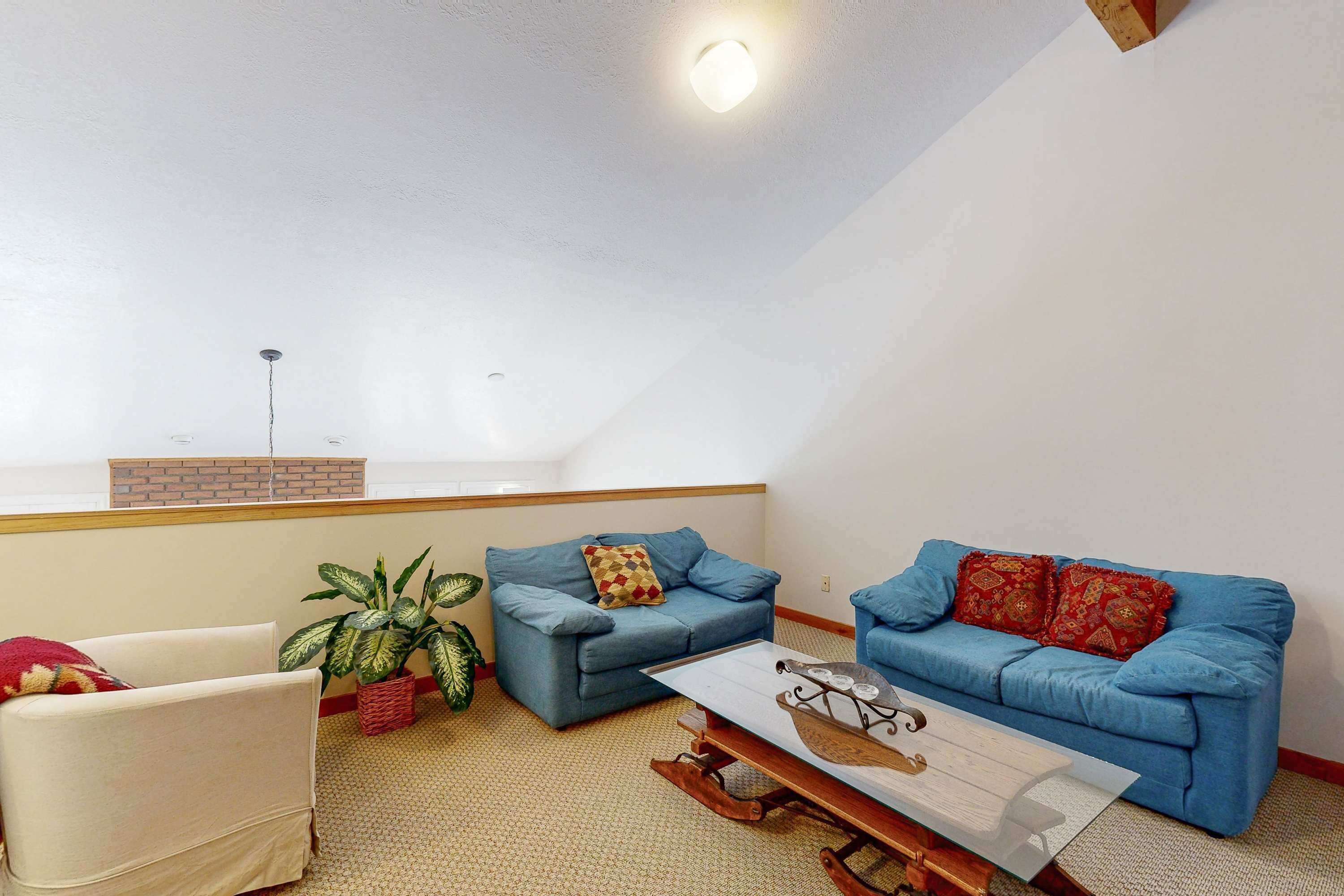 A living room with two blue sofas, a white armchair, a coffee table, and a plant.