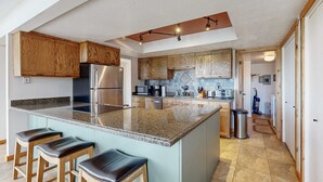 Eine Küche mit Holzausbau, einem Edelstahlkühlschrank, einer Granitarbeitsplatte und drei Barhocker.