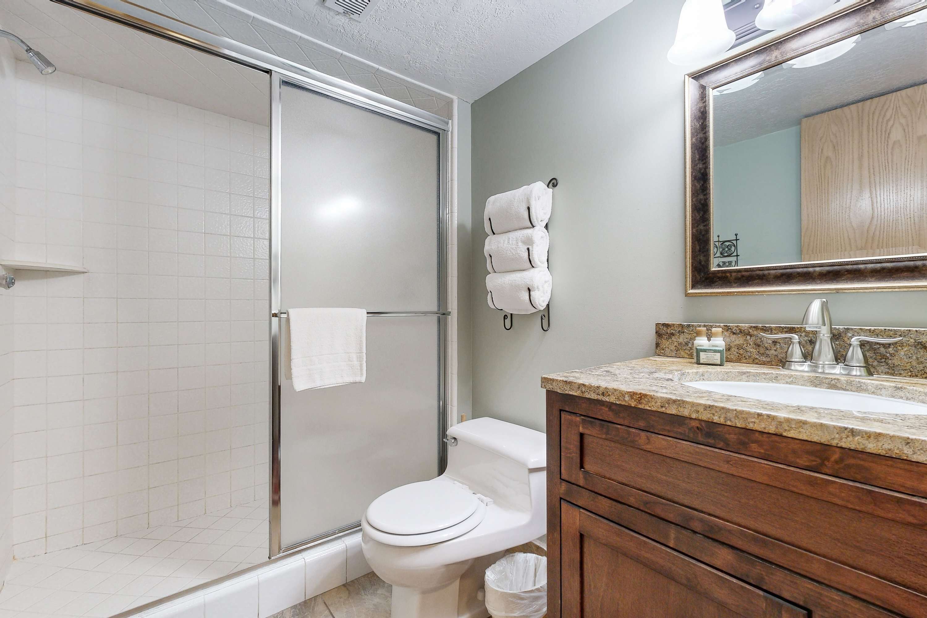 A bathroom with a glass shower enclosure, a toilet, a sink with a mirror, and a towel rack.