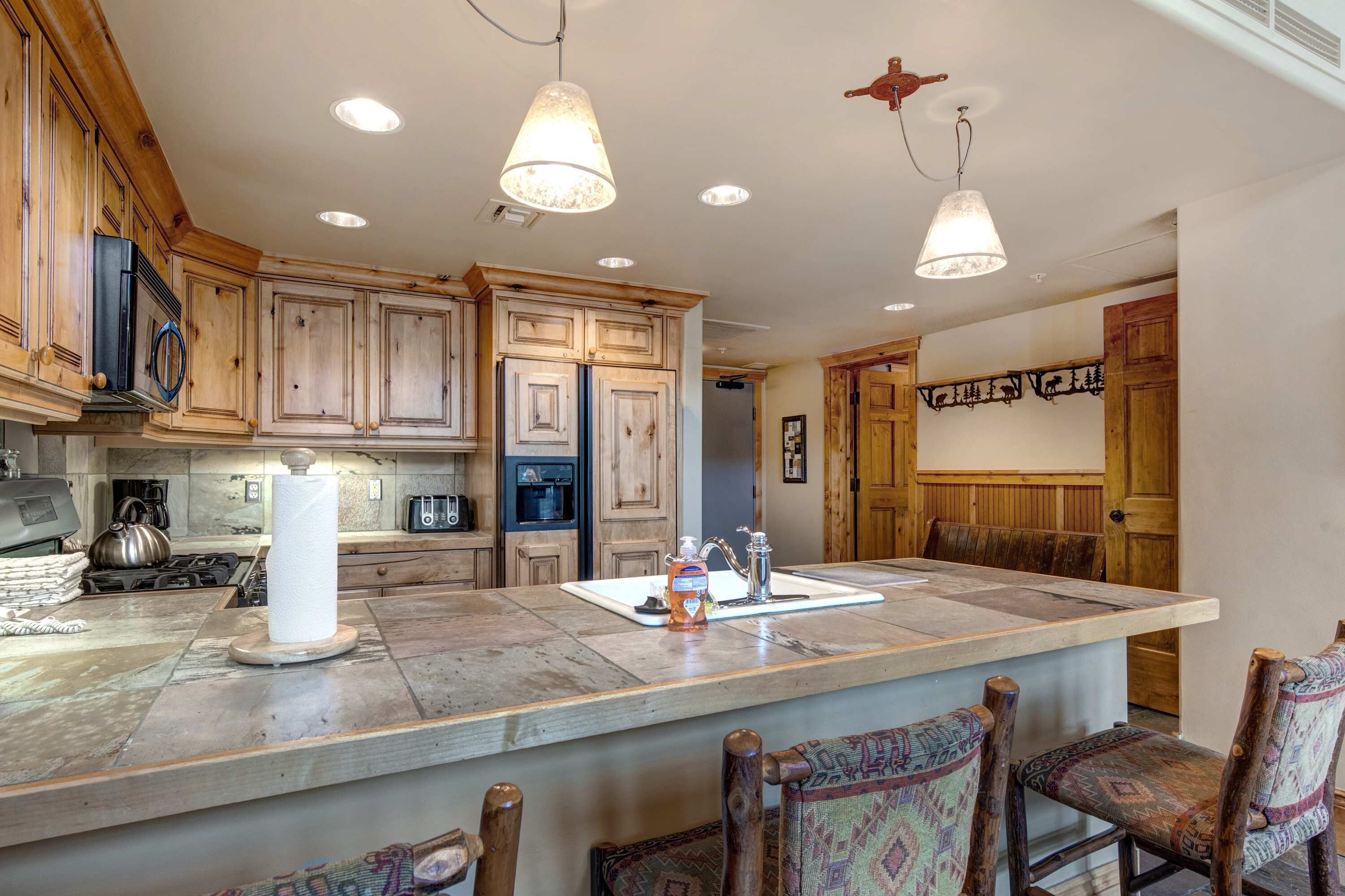 Una cocina con armarios de madera, una isla central, luces colgantes y una zona de comedor con sillas estampadas.