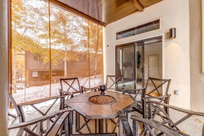 Eine überdachte Terrasse mit einem runden Tisch, Stühlen und einer Feuerstelle.
