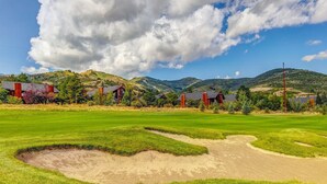 Ein Golfplatz mit Bunkern, blauem Himmel und sanften Hügeln im Hintergrund.