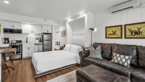 Une pièce moderne et bien éclairée, comprenant un lit, un canapé en cuir, un coin repas et une kitchenette.