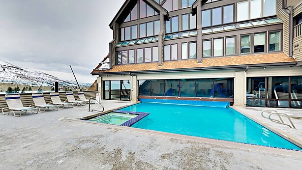 Un bâtiment moderne doté d’une piscine, de chaises longues et offrant une vue sur des montagnes enneigées.