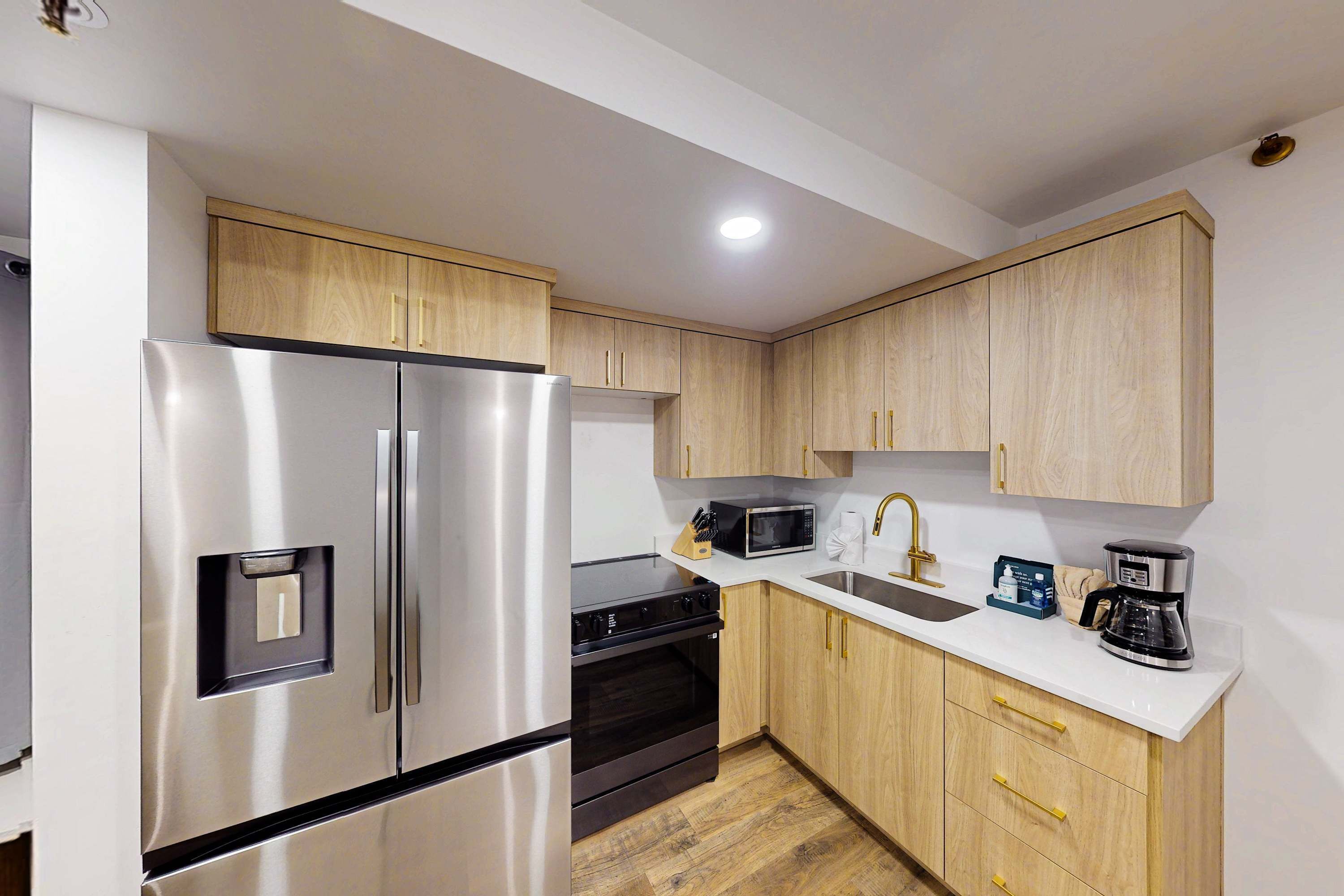 A modern kitchen with stainless steel appliances, wooden cabinets, a white countertop, and a built-in oven.