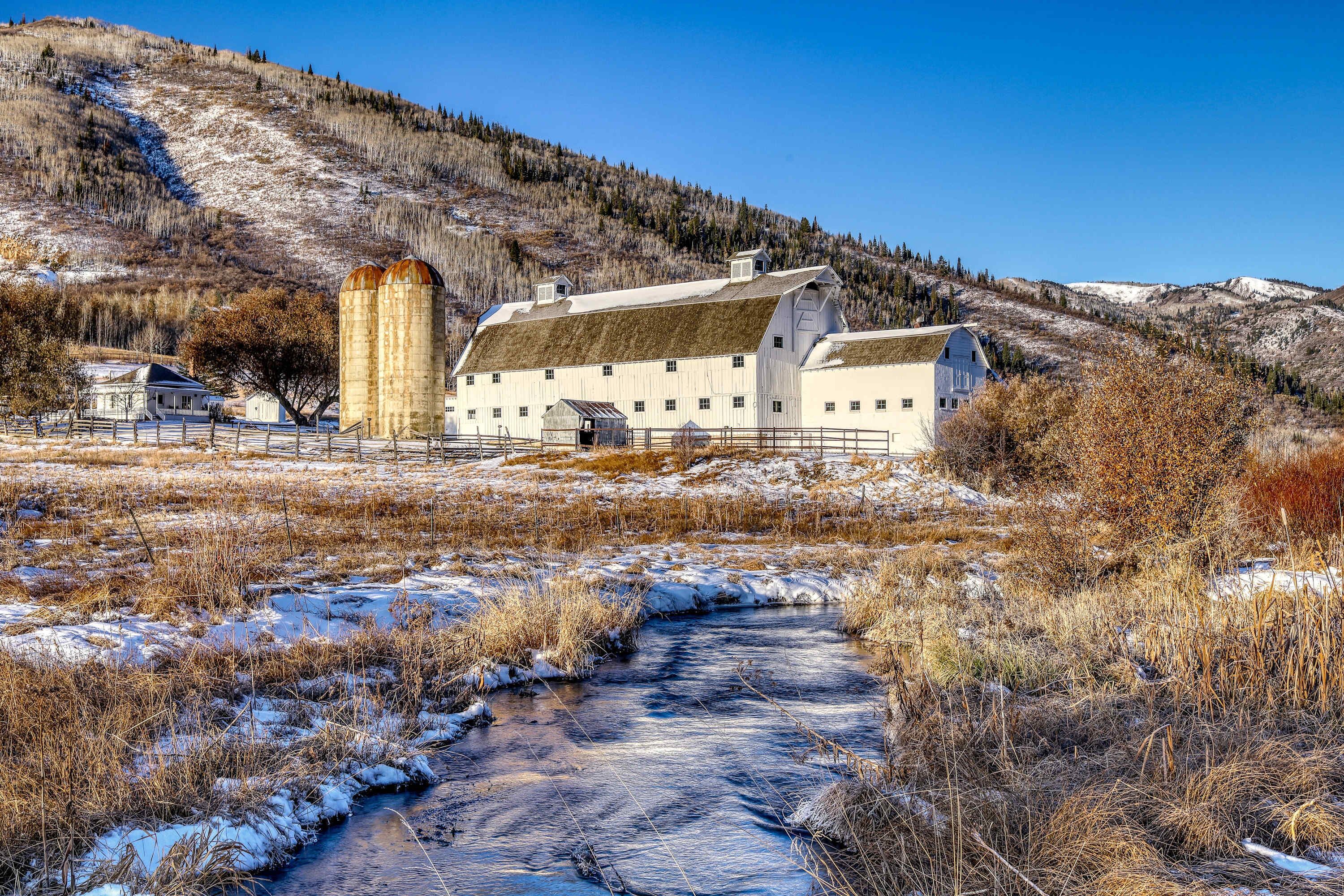 Un paysage rural avec une grange, une petite maison et un ruisseau.