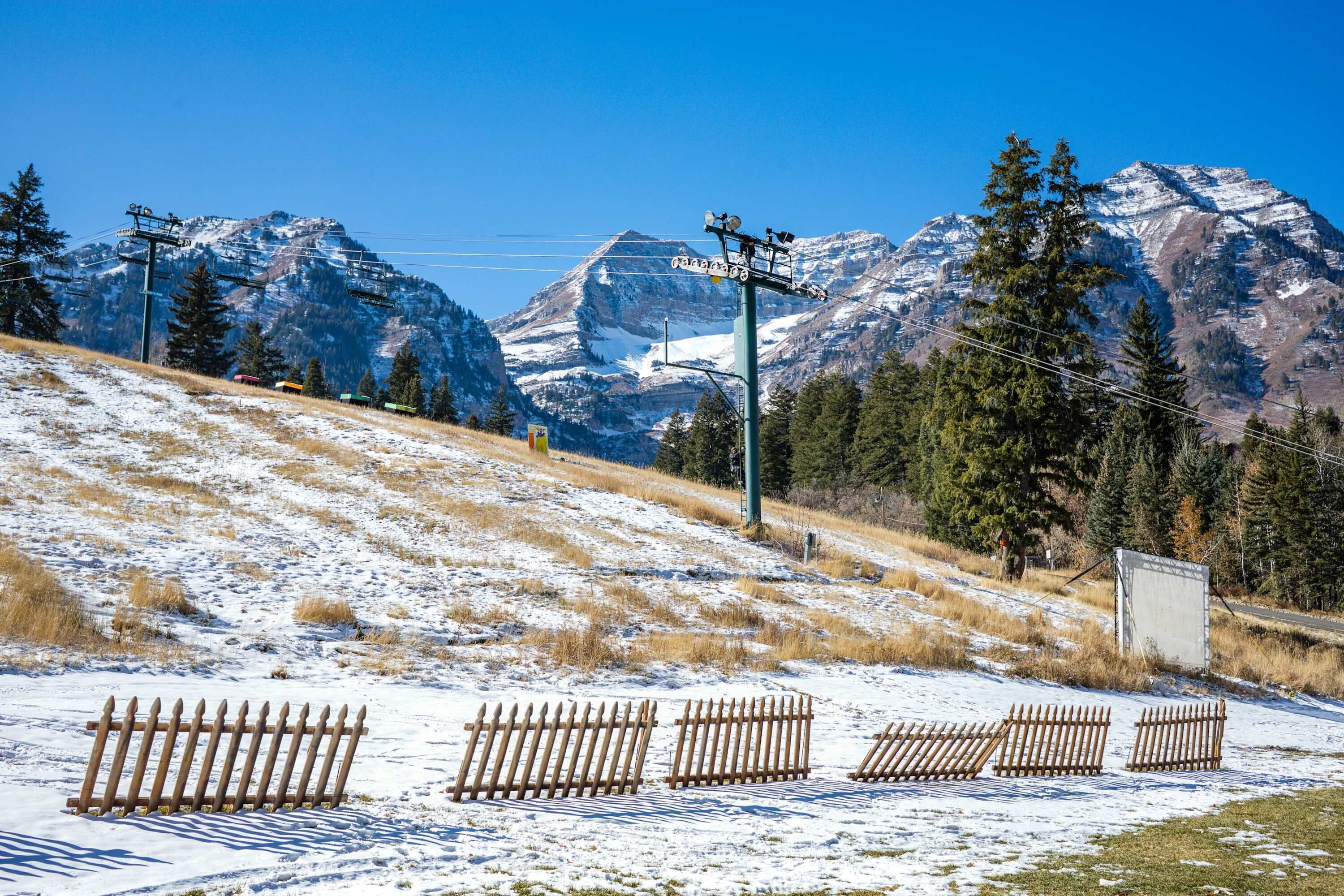 A snow-covered landscape with a ski lift, mountains, and a wooden fence.