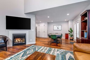 A modern living room with a fireplace, a flat-screen TV, a dining area, and a bookshelf.