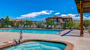 A swimming pool with lounge chairs and a covered area, surrounded by a fence and buildings in the background. - Ski view condo with fast WiFi, private grill, easy ski access, pool, & hot tub (Park City)