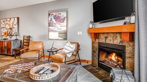 A living room with a fireplace, a television, and a large abstract painting. - Ski view condo with fast WiFi, private grill, easy ski access, pool, & hot tub (Park City)