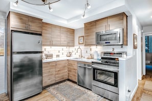 A modern kitchen with stainless steel appliances, wooden cabinets, and a tiled backsplash. - Golf Course Front Condo with Shared Outdoor Pool, Hot Tub, & High-Speed WiFi (Park City)