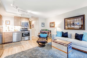A modern living room with a sofa, a coffee table, a massage chair, and a dining area with a microwave and oven. - Golf Course Front Condo with Shared Outdoor Pool, Hot Tub, & High-Speed WiFi (Park City)