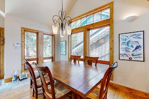A dining area with a wooden table and chairs, large windows, a chandelier, and a framed fish illustration on the wall. - Ski-In, Ski-Out on Park City's 'Gold Coast' - Private Hot Tub - Walk to Dining (Park City)