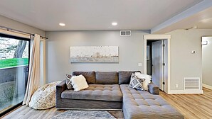 A modern living room with a sectional sofa, a large window with curtains, a ceiling light, and a door leading to another room. - Short walk to Park City lifts (Park City)