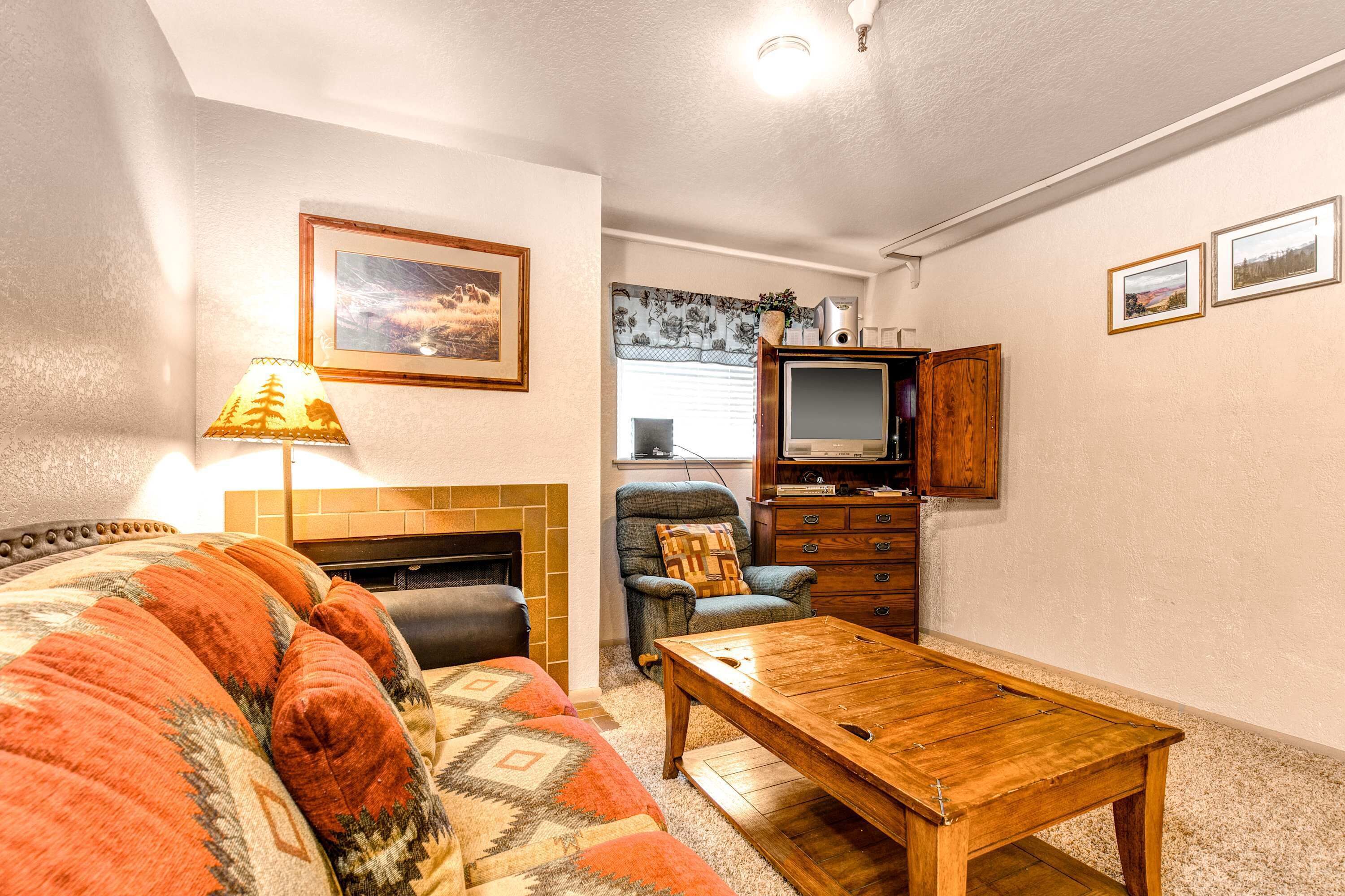 Uma sala de estar com sofá, mesa de centro de madeira, lareira, televisão e um armário.