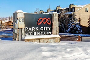 Schild für Park City Mountain mit Logo, umgeben von Schnee und Gebäuden.