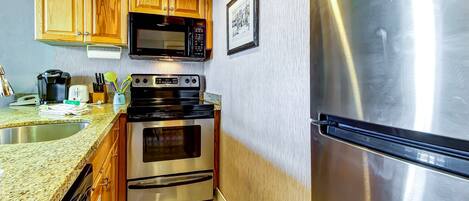 Una cucina con mobili in legno, un frigorifero in acciaio inossidabile, un forno a microonde, un forno e un lavello.