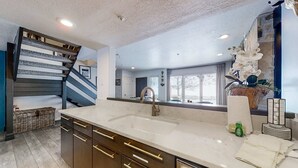 Una cocina moderna con una isla grande, un lavaplatos empotrado y una escalera que conduce a otro nivel.