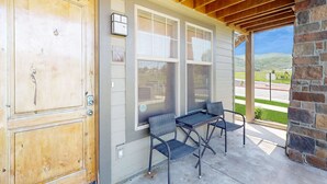 A covered porch with two chairs and a table, a wooden door, and a brick wall. - Redstone Center Gem - Walk to Shops, close to Ski Shuttle Stop (Park City)