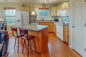 Una cocina con armarios de madera, una isla central con taburetes, un refrigerador, un microondas y vistas al exterior a través de una ventana.