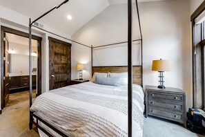 Un lit à baldaquin avec une tête de lit en bois, des tables de chevet avec des lampes, une armoire et un miroir.