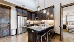 Uma cozinha moderna com armários escuros, eletrodomésticos em aço inoxidável, uma ilha central com banquetas e iluminação pendente.