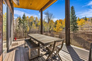 Eine Holzterrasse mit Tisch und Stühlen mit Blick auf einen Wald im Herbstlaub.