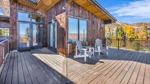 Puinen mökki, jossa on terassi, suuret ikkunat ja Adirondack-tyyliset puutarhatuolit.