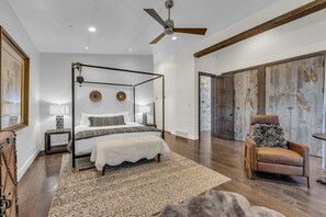 Ein Bett mit Baldachin, weiße Bettdecke, Holzboden, Deckenventilator und eine rustikale Holztür.