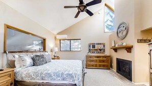 Quarto com cama, mesa de cabeceira, cômoda, espelho, lareira e ventilador de teto.