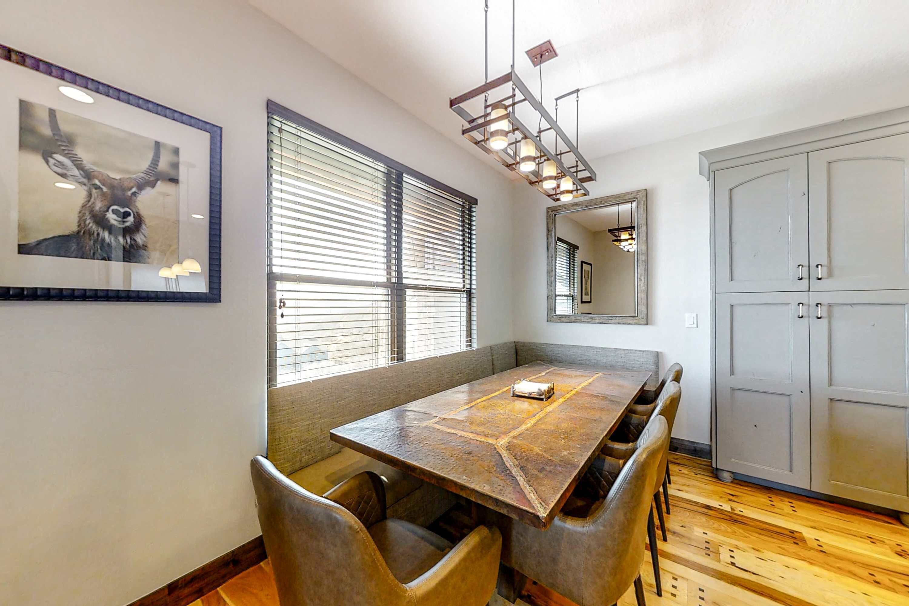 A dining area with a wooden table and chairs, a large window with blinds, a framed animal picture, and a cabinet.